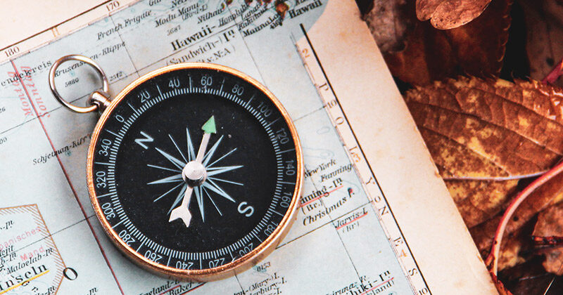 Compass laying on a map with fall leaves in the background